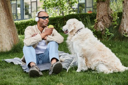 A disabled African American man with myasthenia gravis syndrome sits beside a friendly Labrador dog on lush grass.