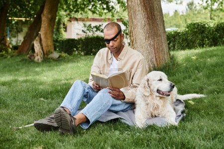 An African American man with myasthenia gravis sits in the grass reading while a loyal Labrador dog sits beside him.