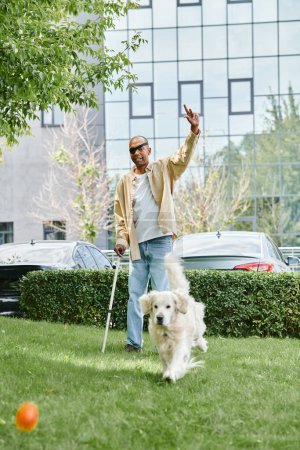 Ein behinderter afroamerikanischer Mann mit Myasthenia gravis geht mit einem Labrador-Hund auf einem grünen Feld spazieren.