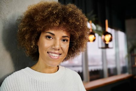 A smiling African American woman with a voluminous afro poses for the camera in a modern cafe, radiating happiness.