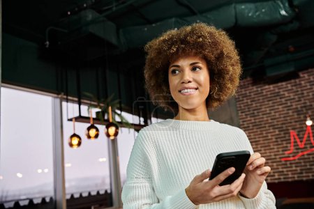 A stylish African American woman holding a smartphone in her hands in a modern cafe.