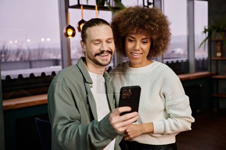 Foto de Un hombre y una mujer afroamericana absortos en un teléfono celular en un café moderno. - Imagen libre de derechos