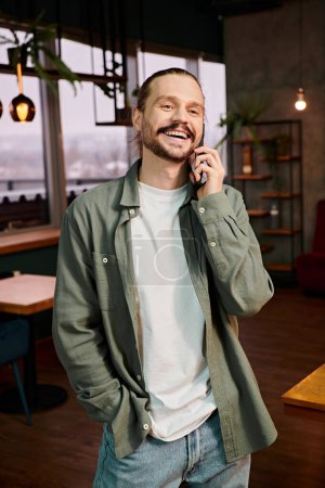 Un homme, dans un restaurant moderne, parle animément sur son téléphone portable tout en se tenant au milieu de l'atmosphère animée.