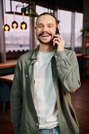 Téléchargez les photos : Un homme debout dans un restaurant occupé, absorbé par une conversation sur son téléphone portable. - en image libre de droit