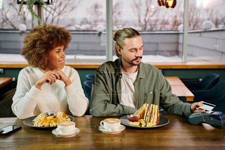 Eine afroamerikanische Frau und ein Mann sitzen an einem Tisch und genießen gemeinsam eine Mahlzeit in einem modernen Café.