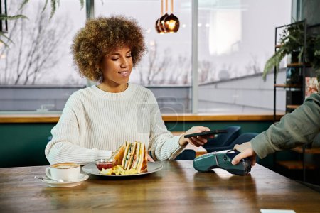 Téléchargez les photos : Une Afro-Américaine s'assoit à une table, dégustant une assiette de nourriture dans un café moderne. - en image libre de droit
