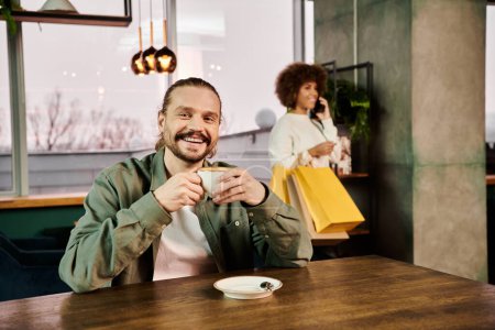 Téléchargez les photos : Homme assis à une table, profondément dans la pensée, tenant une tasse de café dans un café moderne confortable. - en image libre de droit