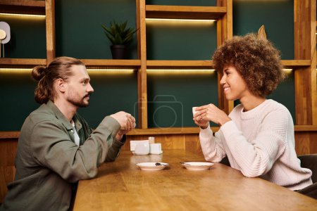An African American woman and man sitting at a table in a modern cafe, enjoying cups of coffee together.