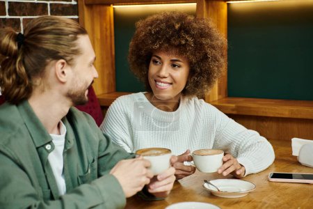 Eine afroamerikanische Frau und ein Mann sitzen an einem Tisch und genießen Tassen Kaffee in einem modernen Café-Ambiente.