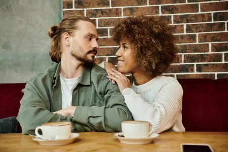 Eine afroamerikanische Frau und ein Mann sitzen an einem Tisch und genießen Tassen Kaffee in einem modernen Café-Ambiente.