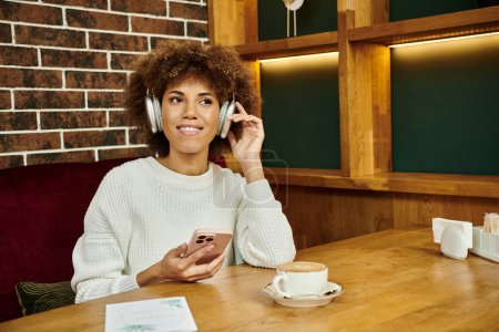 Téléchargez les photos : Une Afro-Américaine est assise à une table de café, parlant sur son téléphone portable, engagée dans une conversation. - en image libre de droit