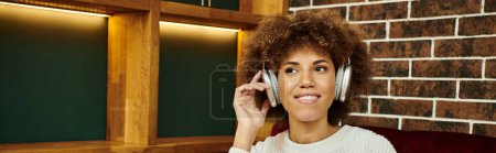 Photo for An African American woman wearing headphones in a modern cafe. - Royalty Free Image