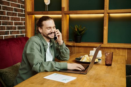 A man, seated at a table in a modern cafe, is engrossed in a phone conversation.