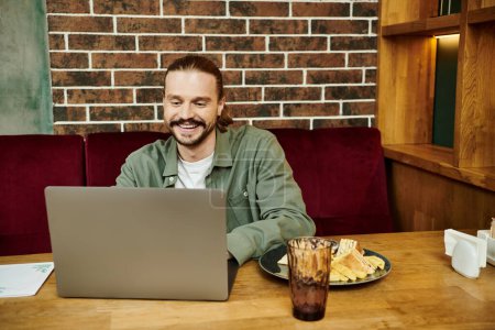 Un homme assis à une table, concentré sur son ordinateur portable, dans un café moderne.