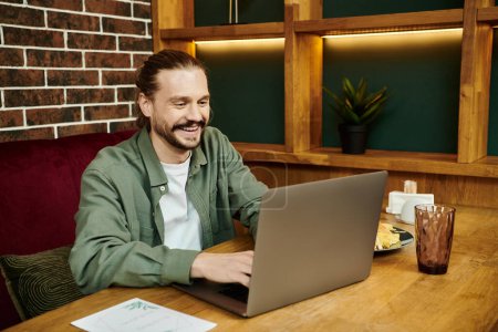 A man intensely focused, uses a laptop at a table in a modern cafe.