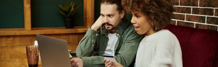 Téléchargez les photos : Une femme afro-américaine et un homme assis dans un café moderne, absorbé comme ils regardent tous les deux un écran d'ordinateur portable. - en image libre de droit