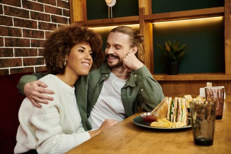 Foto de Un hombre y una mujer de ascendencia afroamericana se sientan juntos en una mesa en un café moderno, conversando. - Imagen libre de derechos