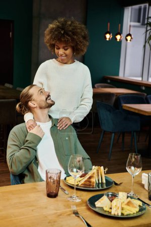 An African American woman and a man are engaged in conversation while sitting at a table in a modern cafe.