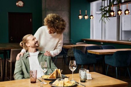 Téléchargez les photos : Une femme afro-américaine et un homme sont engagés dans une conversation autour d'un repas dans un café moderne élégant. - en image libre de droit