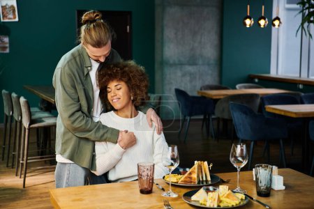 Eine afroamerikanische Frau umarmt einen Mann in einem gemütlichen Restaurant mit modernem Dekor.