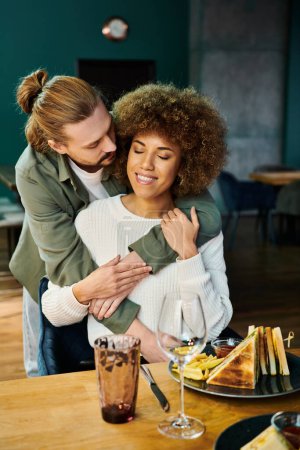 Eine afroamerikanische Frau und ein Mann umarmen sich an einem Tisch in einem modernen Café innig und drücken Liebe und Verbundenheit aus.