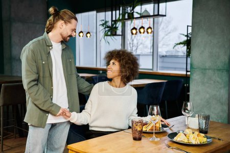 A stylish African American woman and a man stand together by a table in a modern cafe.