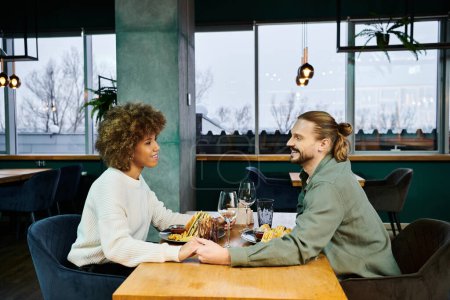 Una mujer afroamericana y un hombre disfrutan de una comida juntos en un café moderno, comprometidos en la conversación y la risa.