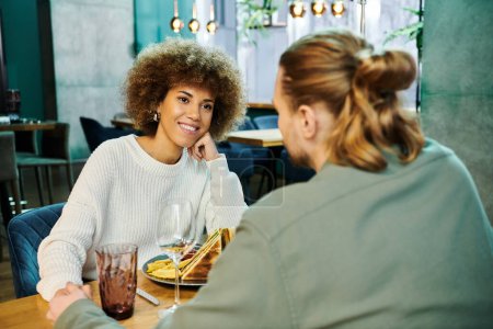 Une femme afro-américaine élégante est assise à une table avec une assiette de nourriture magnifiquement préparée dans un café moderne.