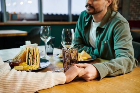 Foto de Una mujer afroamericana y un hombre están sentados en una mesa, con copas de vino en la mano, comprometidos en la conversación en un café moderno. - Imagen libre de derechos