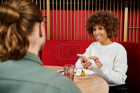 Eine afroamerikanische Frau sitzt an einem Tisch und genießt einen Teller mit leckerem Essen in einem modernen Café-Ambiente.