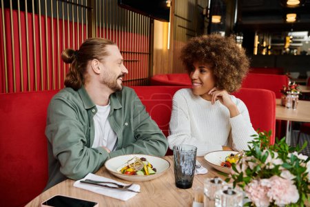 An African American woman and a man enjoying a meal at a table in a modern cafe.