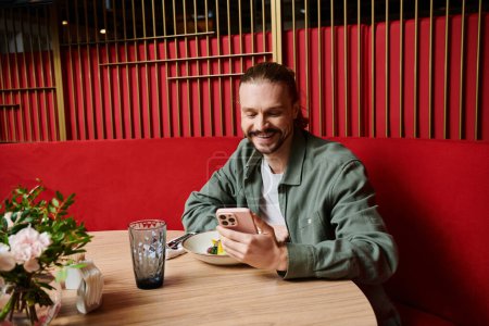 Ein Mann sitzt an einem Tisch, in sein Handy vertieft in einem modernen Café.