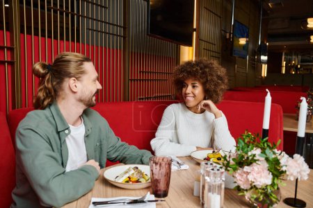 Téléchargez les photos : Une femme afro-américaine et un homme dégustent un repas ensemble à une table de restaurant élégante. - en image libre de droit