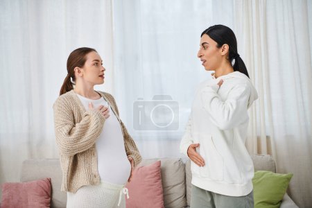 Eine schwangere Frau sitzt bei Elternkursen in einem gemütlichen Wohnzimmer neben ihrem Trainer auf einem Sofa.