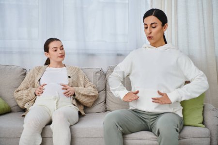 A pregnant woman and her trainer sit atop a couch during a parents course, engaged in conversation.