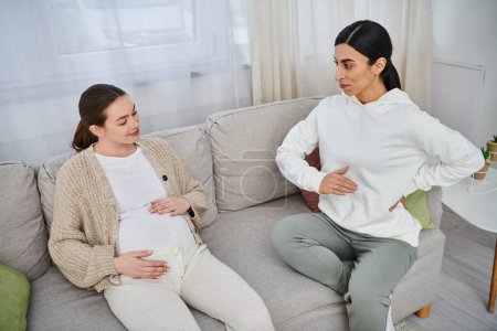 A pregnant woman sits on a couch next to her trainer during parents courses, mirroring each other.