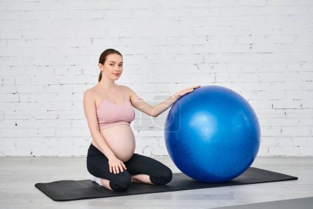 Pregnant woman in yoga pose on mat with exercise ball