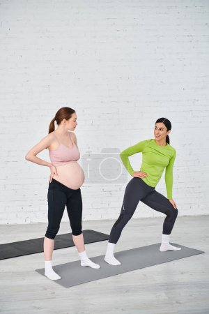 Foto de Dos mujeres embarazadas de pie lado a lado, una entrenando a la otra durante un curso de padres, ambos mostrando fuerza y unidad. - Imagen libre de derechos