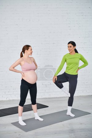 Pregnant woman in yoga pose is joined by coach during parents courses for dual maternity workout.