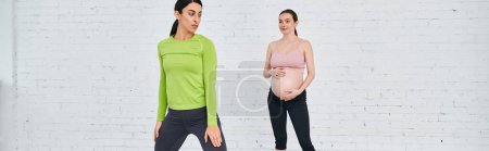 Una mujer está de pie junto a una mujer embarazada durante un curso de los padres, apoyándola y guiándola a través de ejercicios.