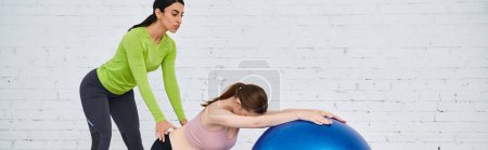 Foto de Una mujer embarazada ejerce con gracia sobre una pelota de ejercicio azul con su entrenador durante los cursos de los padres. - Imagen libre de derechos