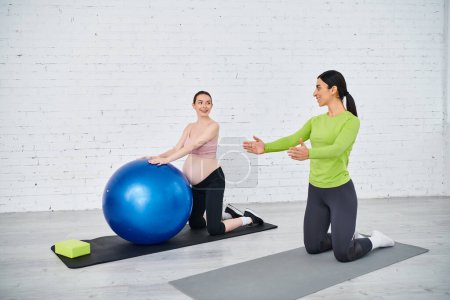 Two women, one pregnant, are performing exercises on exercise balls under the guidance of a coach during parents courses.