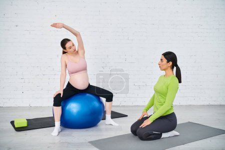 A pregnant woman finds balance and strength as she sits atop a blue fitness ball during parent courses with her coach.