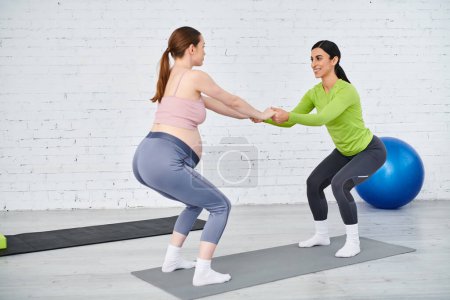 Two women, one pregnant, stand gracefully on a yoga mat, exuding strength and balance in a serene setting.