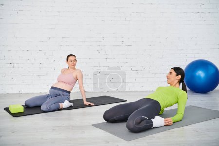 Una mujer embarazada y su entrenador participan en una sesión de yoga pacífica sobre esteras, que encarna la fuerza y la gracia.