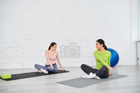 Photo for A pregnant woman exercises with her coach during a parents course, sitting on yoga mats in a serene setting. - Royalty Free Image