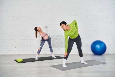 Foto de Un entrenador y una mujer embarazada realizan ejercicios de yoga sobre esteras durante un curso de padres. - Imagen libre de derechos