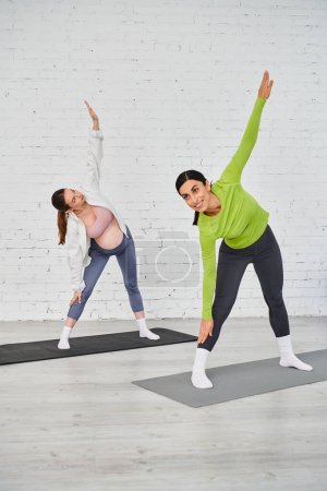 A pregnant woman gracefully practices yoga with her instructor in a serene studio setting.