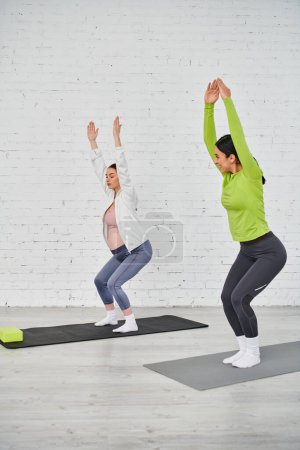 Téléchargez les photos : Un groupe diversifié de femmes, y compris une femme enceinte, pose de yoga frappant devant un mur rustique de briques blanches. - en image libre de droit