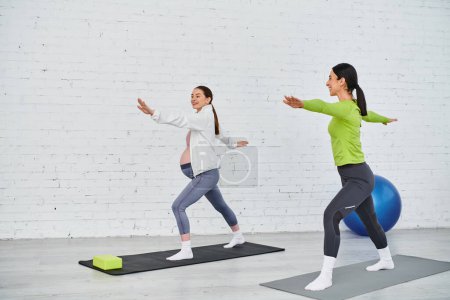 Una mujer embarazada practica yoga con su entrenador durante un curso de padres, de pie uno al lado del otro en colchonetas de yoga.